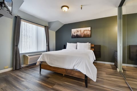 Bright and comfortable bedroom featuring a plush queen bed, natural light, and a cozy sitting area beside the window.