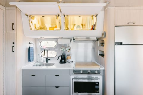 Overhead bins are stocked with coffee supplies, cups, wine glasses, plates, bowls, food storage containers and more! 