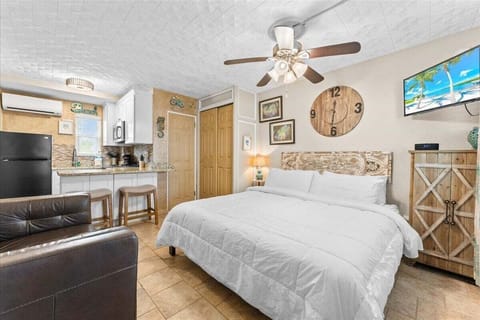 King bed studio with smart TV, ceiling fan, AC unit, and coastal décor — kitchenette and sofa just steps away for a comfortable, laid-back beach getaway.