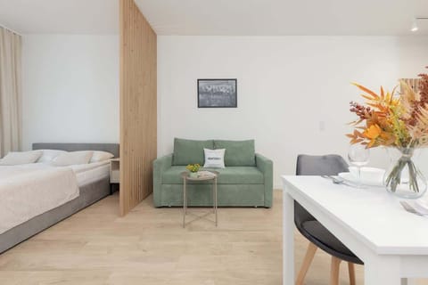 A cozy living area featuring a green sofa, a modern dining table with chairs, and natural wood accents.
