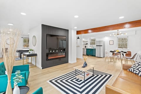 This open-concept living room is the perfect mix of cozy and stylish, featuring a sleek black accent wall with an electric fireplace and a large TV for ultimate relaxation.