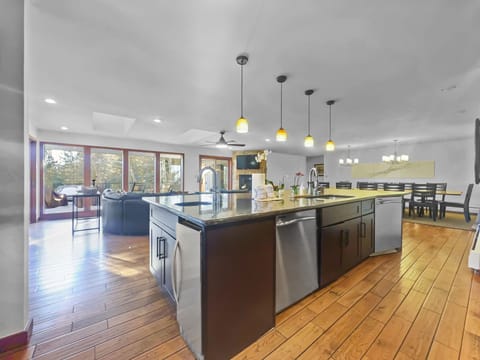 A modern open-concept kitchen with a large island, stainless steel appliances, and pendant lighting. The kitchen opens to a living area with floor-to-ceiling windows and a dining space.