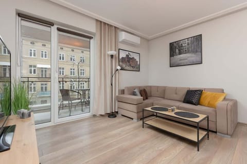 A modern living room with a large window, a cozy beige sofa, a coffee table, and a TV.