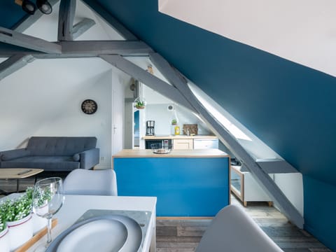 "An open, bright kitchen next to a window, with white and blue walls. In one corner there is a sofa, creating a relaxation area."
