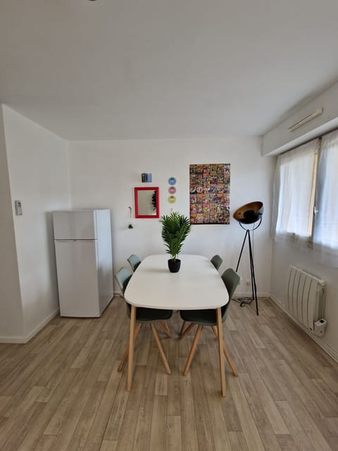 "Discover the dining area in the living room of the Le Square apartment in Le Mans through this photo. You can see the table seating 4, the fridge, the wall decoration, the window and a radiator on the right. A retro design lamp adds a touch of elegance to the space."