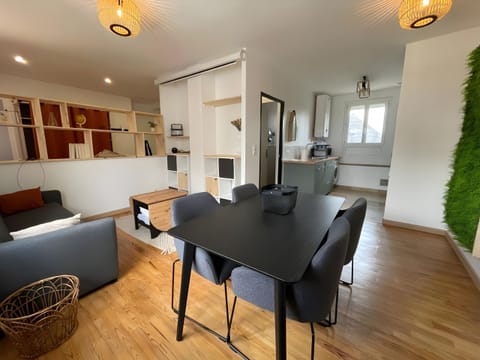 "Discover our dining room at l'Enchantement. Plush sofa, folding coffee table, video projector blind, designer shelves, parquet flooring and a chic dining table intertwined with a subtle glimpse of the kitchen."