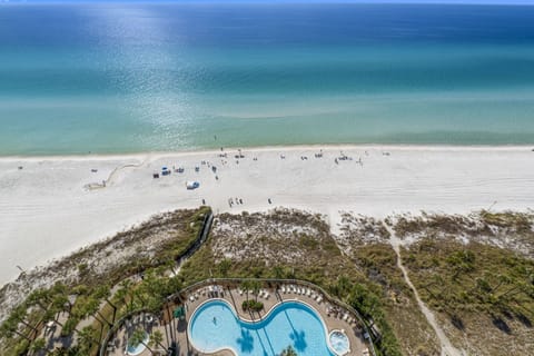 Aerial view of a beachfront pool area with direct access to a white sand beach and clear blue water.