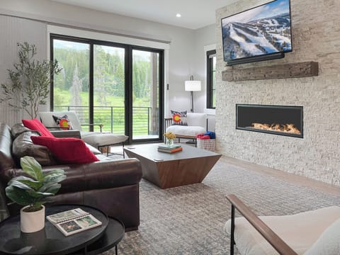 - Kick back in this modern mountain living room with a stone fireplace, plush sofas, and wall mounted TV - Tall glass doors open to outdoor views, letting nature flow in - Bold colors, wood accents, and curated details elevate your downtime
