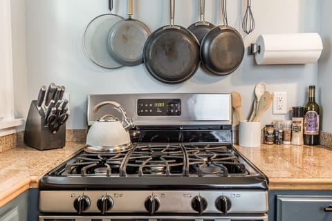 The cooking area featuring a stove with hanging pots and pans, a knife set, and cooking utensils for preparing meals.