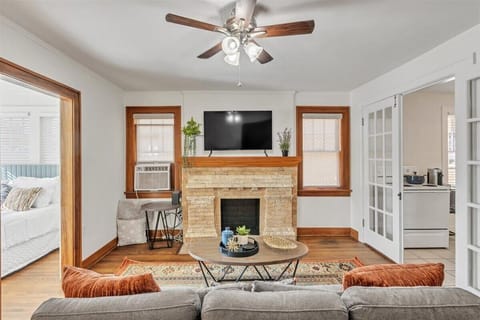 Living room with original hardwood floors, mock fireplace, couch & smart TV.