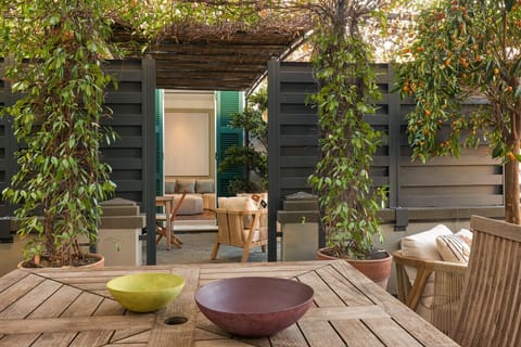 Seamless transition between indoor and outdoor spaces: the dining table under a pergola opens directly to the cozy living area and lush terrace with citrus trees and greenery.