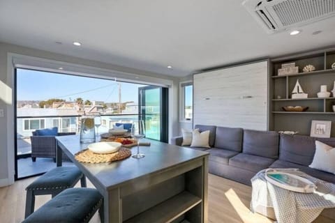 LIVING ROOM – Unwind in the open-concept living room featuring comfortable seating, a flat-screen TV with streaming access, and sliding glass doors that fill the space with natural light and refreshing ocean breezes for a relaxed coastal stay.