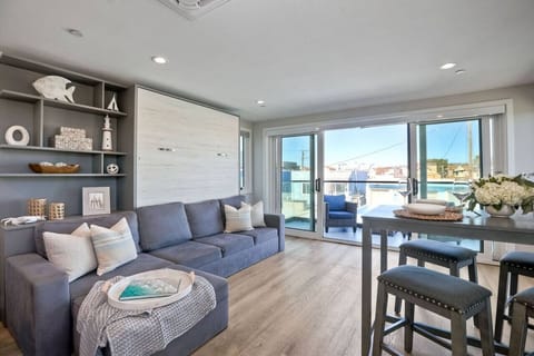 LIVING ROOM – Relax in the open-concept living area with comfortable seating and a flat-screen TV. Sliding glass doors let in plenty of natural light and the signature ocean breeze, creating an easygoing space to unwind.