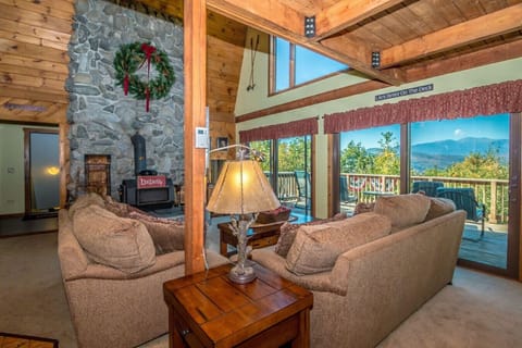 Cozy den with an open floor plan to the kitchen and dining area. Enjoy mountain views through sliders to the deck, a large wood stove for warmth, and a big-screen TV with streaming—perfect for unwinding.