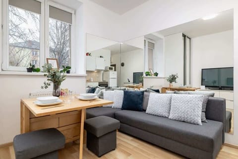 Cozy dining area with a wooden table set for two, positioned next to a comfortable gray sofa with decorative pillows, and a large window letting in natural light.
