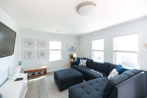 Relax in a sun‑filled open living space featuring a large sectional couch, Smart TV, and coastal décor.
