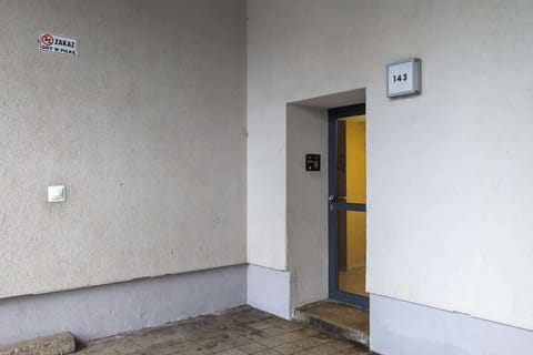 Exterior entrance of the building with a neutral facade and yellow door, giving a glimpse into the quiet residential setting.