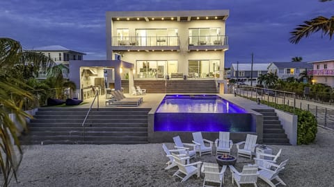 Twilight view of the home, infinity pool, lounge area and fire pit
