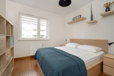 A cozy bedroom with a double bed, white and blue bedding, wooden accents, and soft lighting, creating a comfortable atmosphere.
