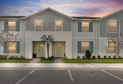 Step outside to enjoy the charming facade adorned with soft blue siding and inviting white trim, framed by lush greenery and delicate trees. The warm glow of evening light enhances the welcoming atmosphere of your vacation home.