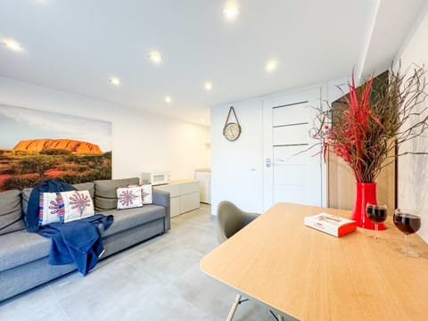 A modern living room with a grey sectional sofa, colorful cushions, and a wooden dining table decorated with vibrant red branches, creating a cheerful and inviting atmosphere.
