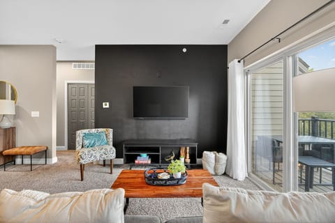Gather in the stylish living area with bold black accent wall, mounted TV, and curated décor. Sliding doors open to a private balcony, extending your living space into the fresh air.