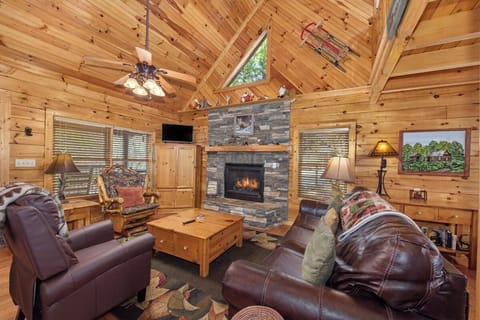 Cozy up by your stone fireplace in this rustic living room with vaulted ceilings and leather seating for mountain getaway relaxation.