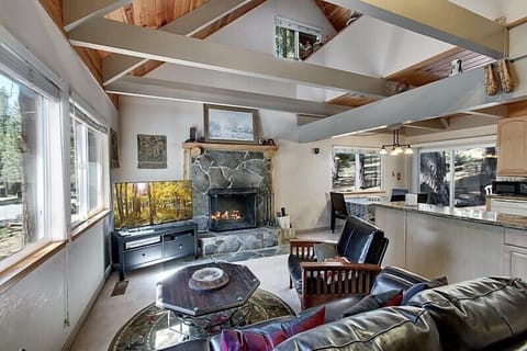 Cozy living room with vaulted ceilings, a stone fireplace, and large windows bringing in natural light.