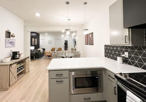 KITCHEN – This kitchen open to the living area is sleek and modern designed for both style and functionality. The black geometric backsplash adds a bold touch, contrasting beautifully with the soft grey cabinetry and white countertops. Stainless steel appliances, including a large refrigerator, dishwasher, and a handy toaster oven, make meal prep and cleanup a breeze. With plen...