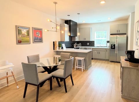 KITCHEN & DINING AREA – This modern kitchen and dining space offers both style and functionality. The sleek glass dining table is complemented by comfortable upholstered chairs, perfect for family meals or casual gatherings. The kitchen features stainless steel appliances, chic cabinetry, and a striking black geometric backsplash. Pendant lighting above the island adds a contem...