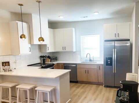 MODERN KITCHEN WITH ISLAND SEATING – This bright, open kitchen is the heart of the home, featuring sleek stainless steel appliances and a spacious layout. The white countertops and cabinetry, paired with modern pendant lighting, create a fresh and welcoming atmosphere. An island with bar stools provides a casual dining option or a perfect spot to gather around while cooking. Eq...