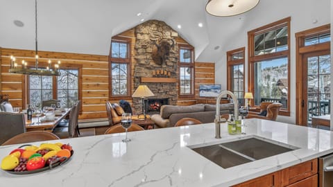 Your open-concept kitchen flows seamlessly into the living area, where crackling fireplace warmth mingles with mountain views through floor-to-ceiling windows.