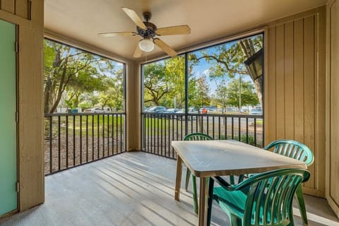 Screened porch with ceiling fan and outdoor seating overlooking trees and parking area.