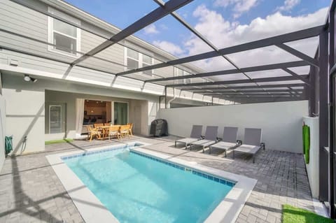 Modern outdoor pool area with lounge chairs and dining space under a screened enclosure