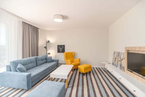 A bright and spacious living room with a gray-blue sofa, a yellow armchair, and a striped rug, complemented by natural light.
