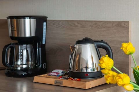 Coffee station with kettle, cups, and a vase with yellow flowers.