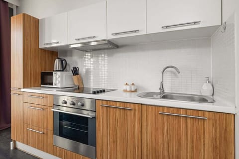 Kitchenette with upper cabinets in white, lower cabinet fronts imitate wood. The kitchen is equipped with a microwave and a refrigerator. 