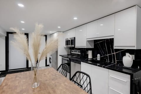 Bright, modern full kitchen with sleek white cabinetry & black marble-effect countertops. Includes stainless steel appliances & a dining table with chairs. Perfect for cooking & enjoying meals. Contemporary design for a comfortable stay.