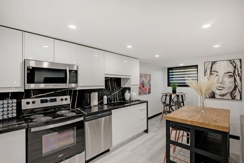 Modern full kitchen with sleek stainless steel appliances, including oven, microwave, & fridge. Features ample counter space & stylish cabinetry. Adjacent island with seating and artwork for a vibrant feel. Perfect for home-cooked meals during your stay.