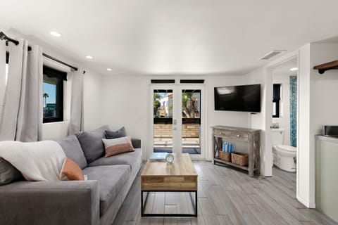 Luminous minimalist Living space features a large mid-century Sofa Bed with soft furnishings, a coffee table, and a Smart TV with cable/satellite, offering direct access to the Outdoor space.