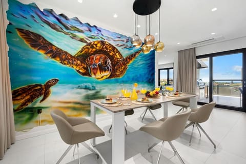 Enjoying a meal surrounded by the serene beauty of a sea turtle mural in this stunning dining room. Elegant chandelier adds a touch of glamour, while the table and chairs invite you to savor every moment of your meal.