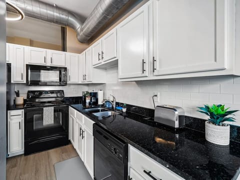 Sleek kitchen featuring granite countertops and modern black appliances - White cabinets with chrome handles and clean subway tile backsplash - Essentials like toaster, dishwasher, and coffee maker ready for use