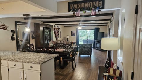 Open-concept dining and living area with dark wood furniture, granite countertop, patterned armchair, and sliding glass doors.
