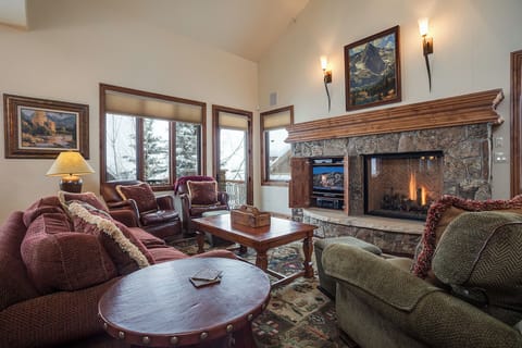 Sink into plush sofas by your crackling stone fireplace, where mountain artwork and warm lighting create the perfect retreat after adventure-filled days.