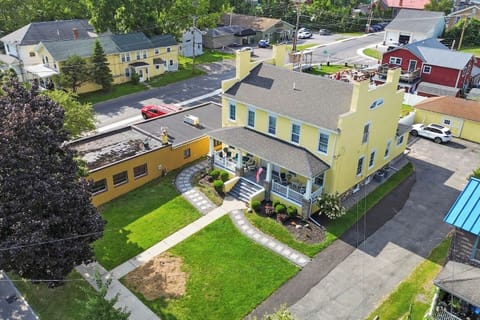 A sun-kissed yellow house, nestled in an open and spacious setting, features a welcoming porch adorned with comfortable seating.