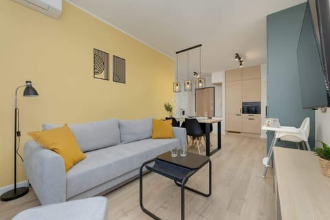 Living room with a light blue sofa, a coffee table, and large artwork on the wall, featuring a yellow accent wall and large windows.