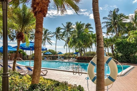 Lounge poolside under blue umbrellas and tropical breezes.