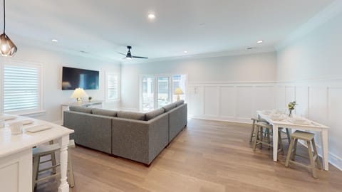 Open-plan living room with comfortable seating, big-screen TV, and natural light streaming through large windows.