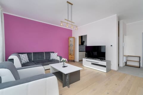 A stylish living room with a bold pink accent wall, a gray sofa set, and a modern entertainment center, creating a vibrant yet elegant atmosphere.

