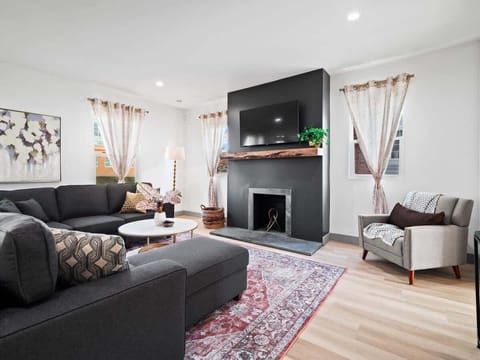 - Bright living room with sectional sofa and flat screen TV - Cozy fireplace accent wall with wood beam detail - Natural light and stylish decor for comfort